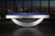 Side view of the Doc & Holliday Poshy Reverse Rainbow Slate Pool Table with Euro Blue Championship felt, matte black rails, and brushed metallic silver base, staged on a concrete floor with a clean modern backdrop wall. Side view of the Doc & Holliday Poshy Reverse Rainbow Slate Pool Table with Euro Blue Championship felt, matte black rails, and brushed metallic silver base, staged on a concrete floor with a clean modern backdrop wall.